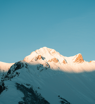 Sommet de montagne enneigée illuminé par le soleil avec un ciel bleu clair en arrière-plan.