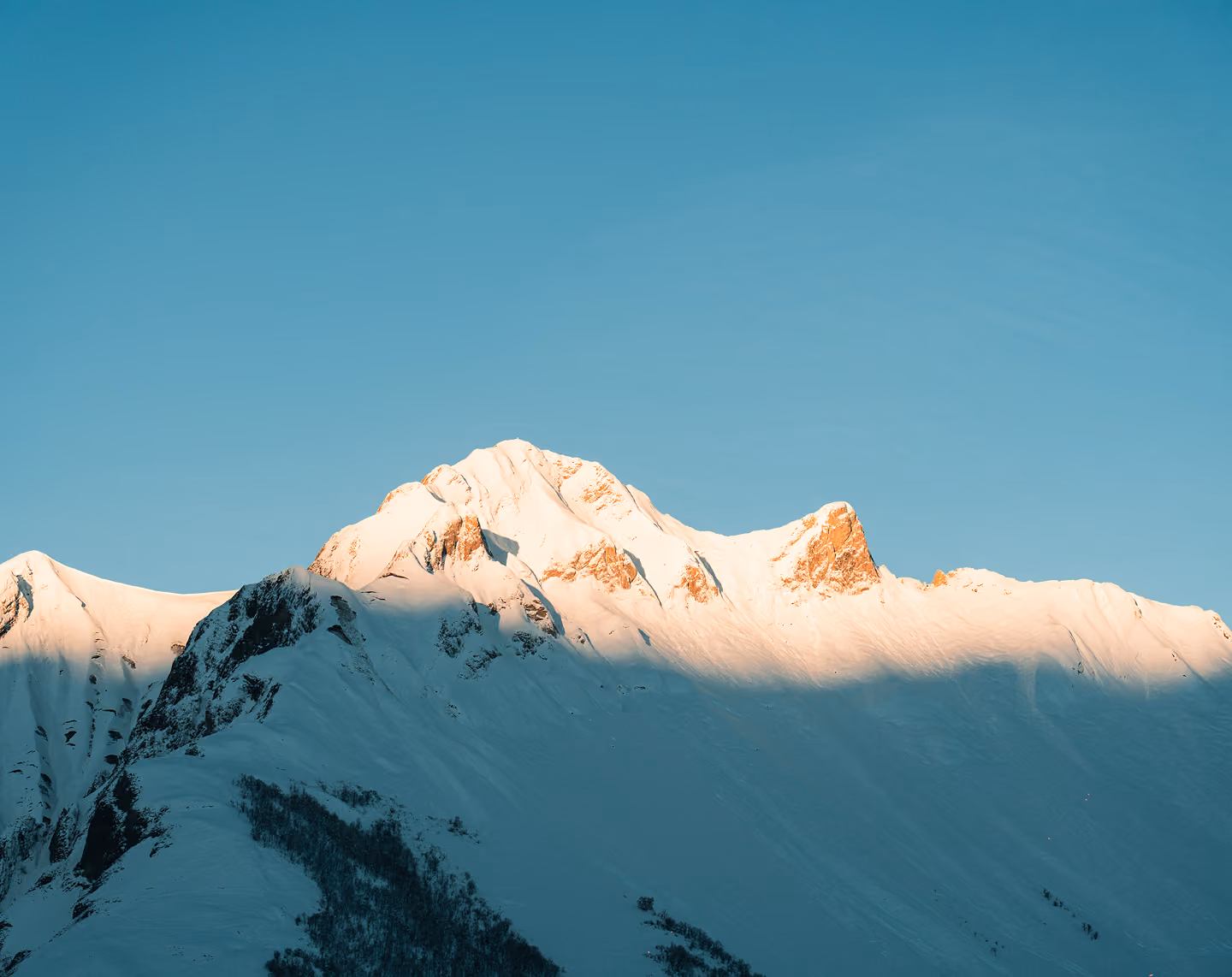 Montagne enneigée éclairée par la lumière du soleil contre un ciel bleu clair.