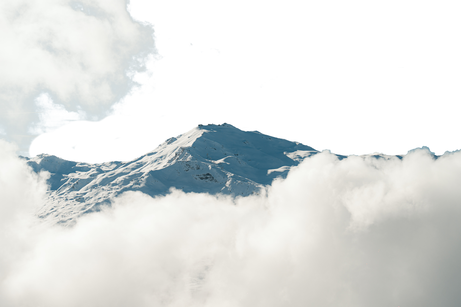 Montagne enneigée avec des sommets visibles au-dessus des nuages et un ciel bleu clair en arrière-plan.