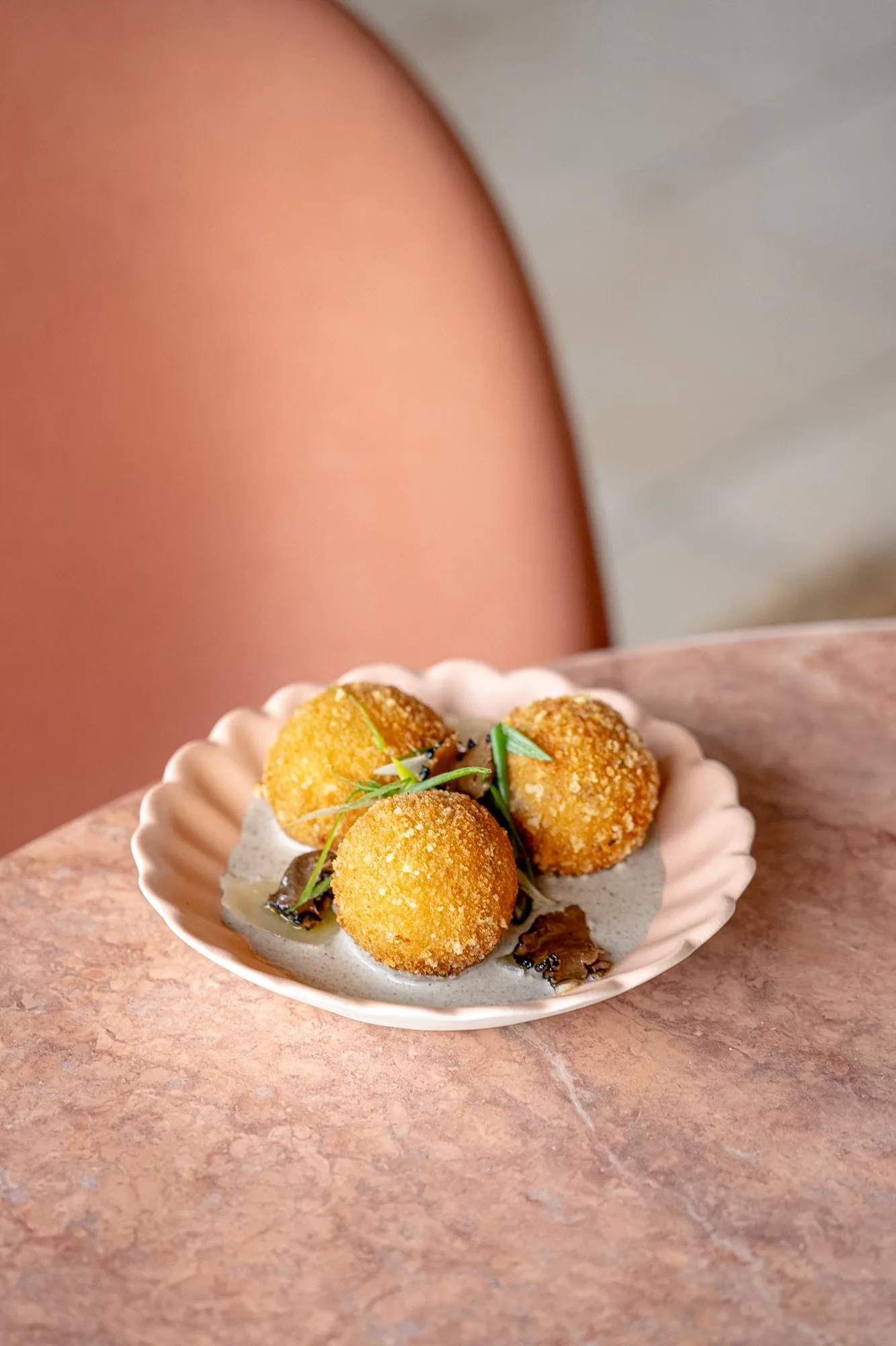Trois croquettes dorées croustillantes servies dans une assiette rose avec une sauce et garnies de fines herbes vertes et de morceaux de champignons.