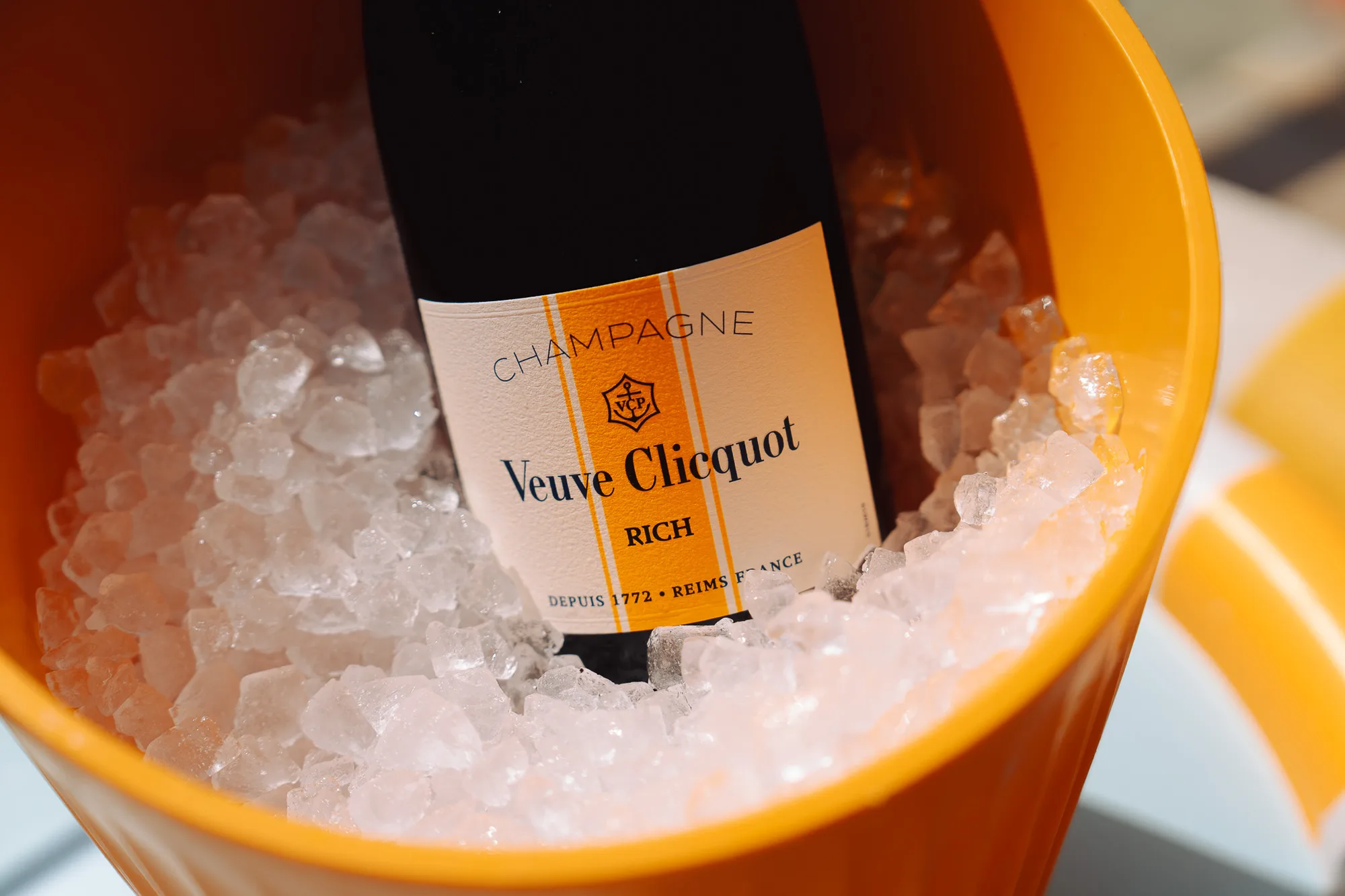 Bouteille de champagne Veuve Clicquot Rich dans un seau à glace orange remplie de glaçons.