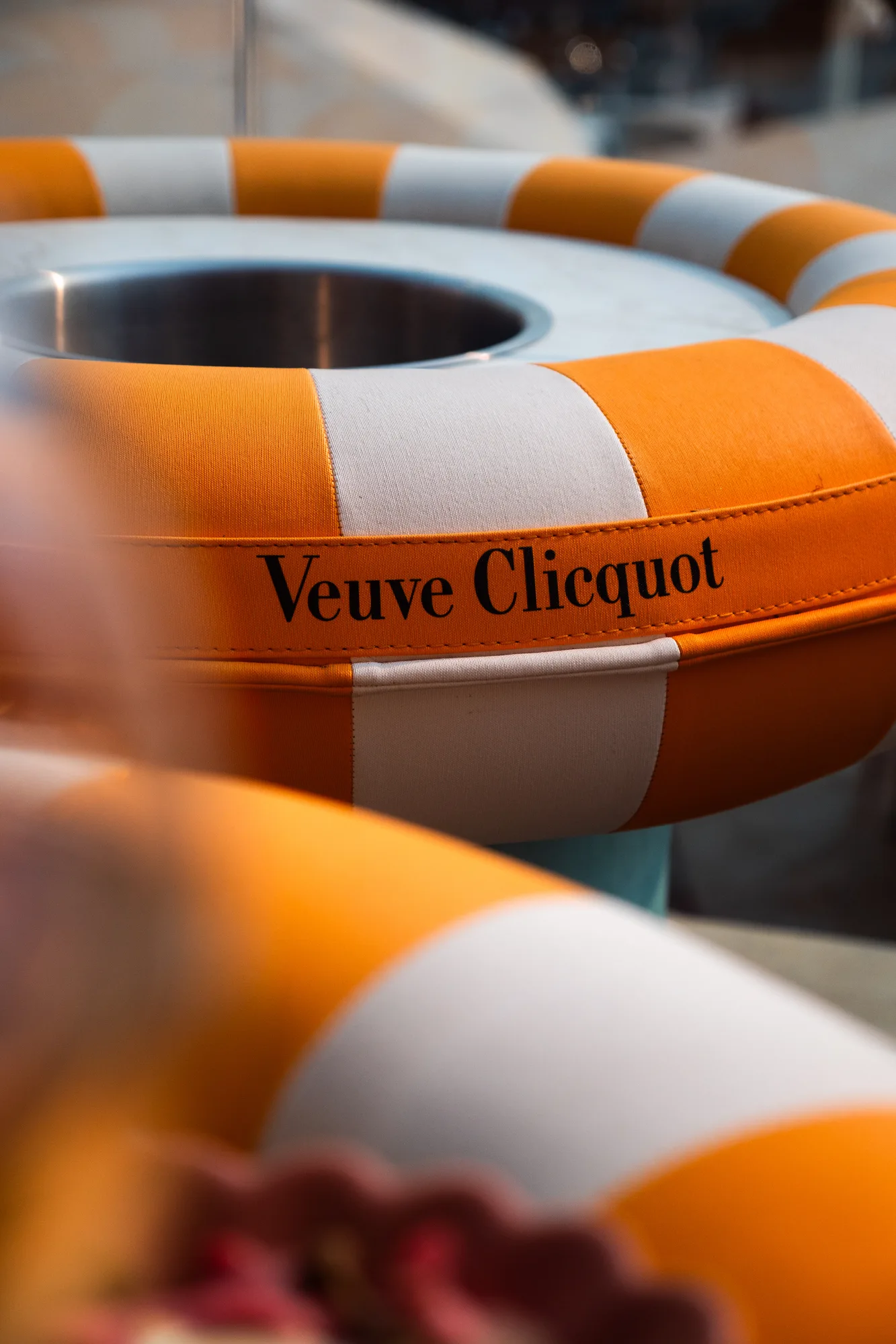 Anneau en tissu orange et blanc avec le texte « Veuve Clicquot » inscrit dessus, entourant un récipient en métal.