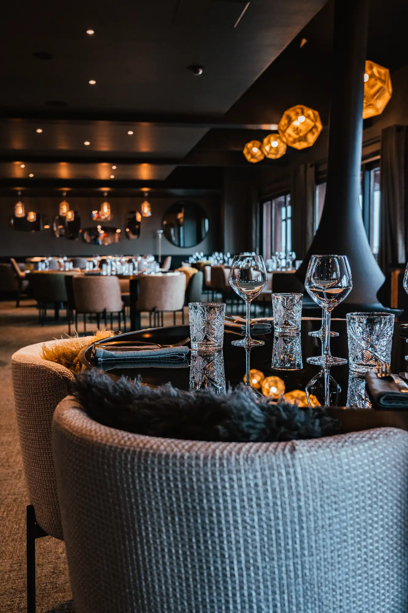 Intérieur élégant d'un restaurant avec des tables en verre noir dressées de verres à vin et verres à eau, chaises rembourrées et éclairage suspendu chaleureux.