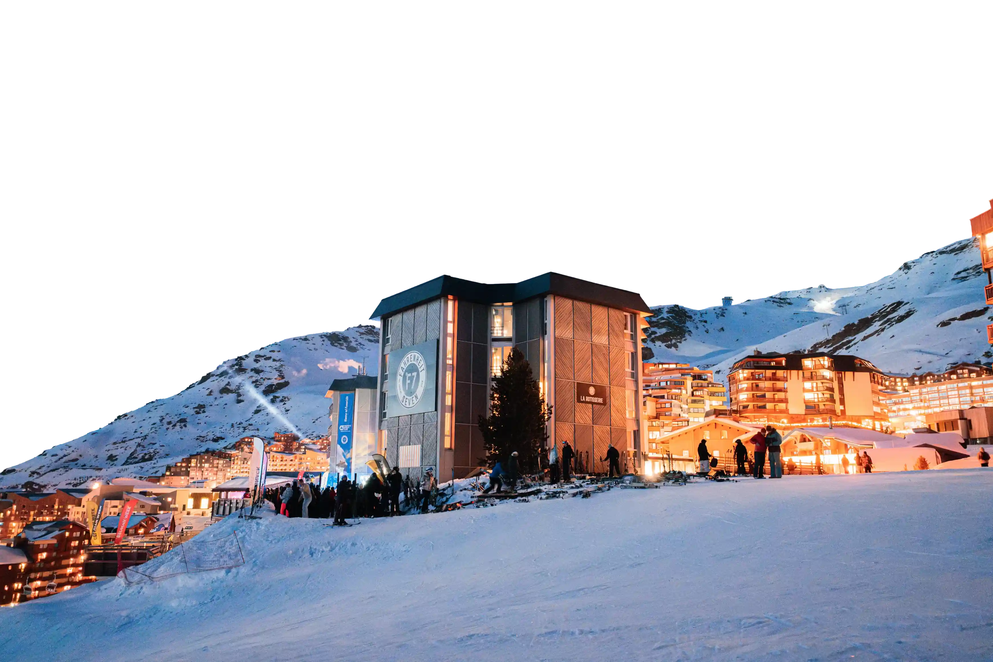 Station de ski animée la nuit avec un bâtiment central marqué F7, des skieurs, et des montagnes enneigées en arrière-plan illuminées par des lumières de la station.