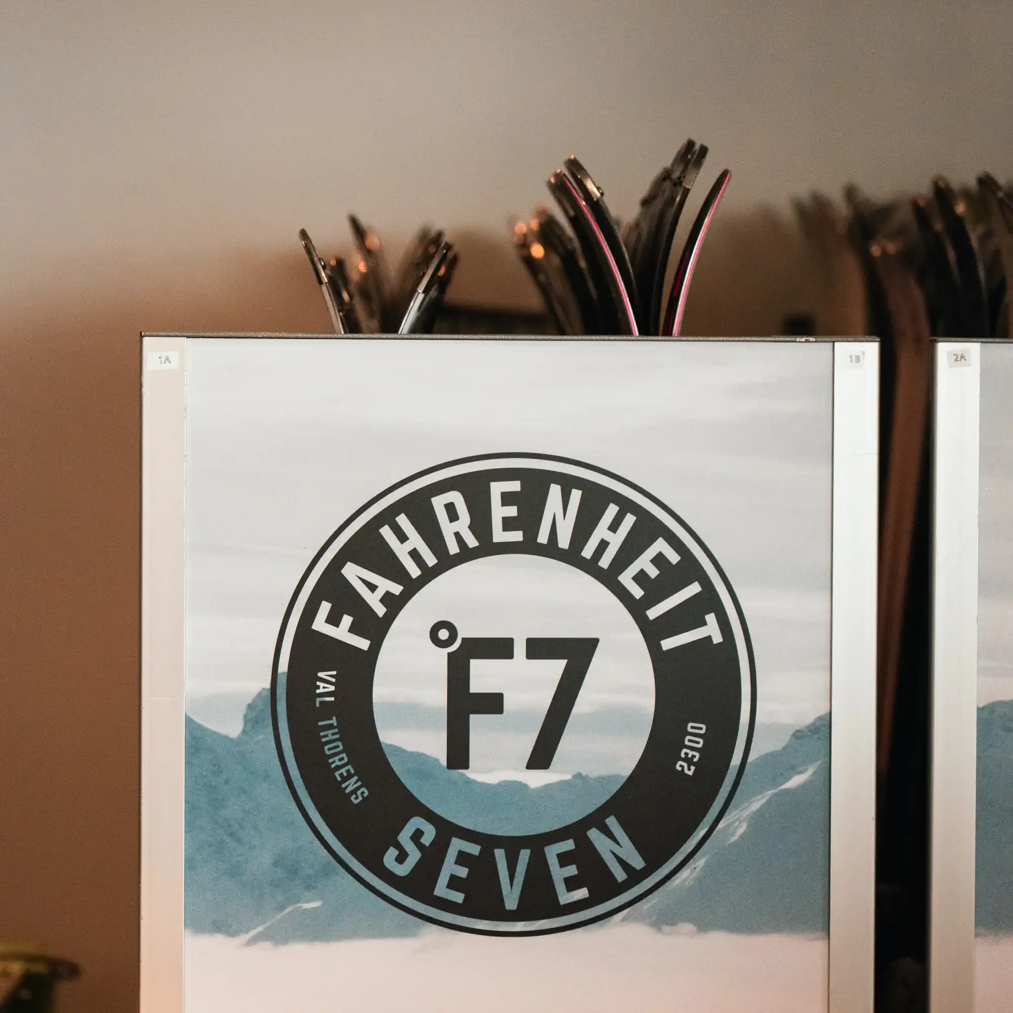 Logo circulaire noir de Fahrenheit Seven avec le texte et le symbole °F7, sur un fond de montagnes bleues et ciel gris.