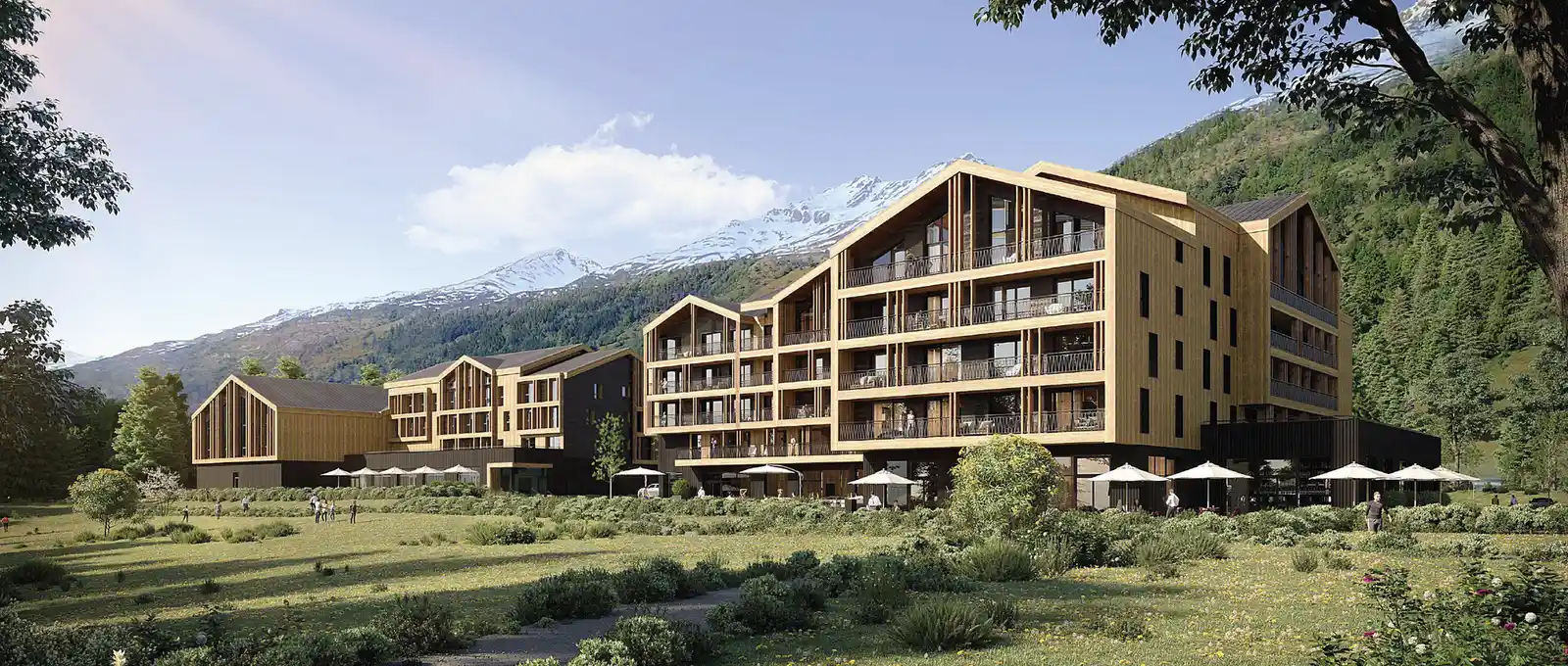 Grand bâtiment moderne en bois avec plusieurs balcons, situé dans un paysage de montagne verdoyant avec des arbres et des personnes sur une pelouse, ciel clair avec quelques nuages.
