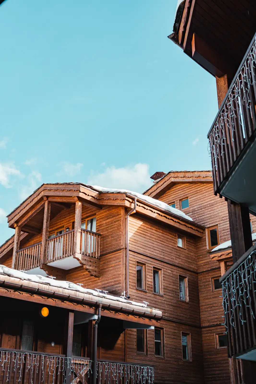 Immeuble en bois avec balcons et gouttières, recouvert légèrement de neige sous un ciel bleu clair.
