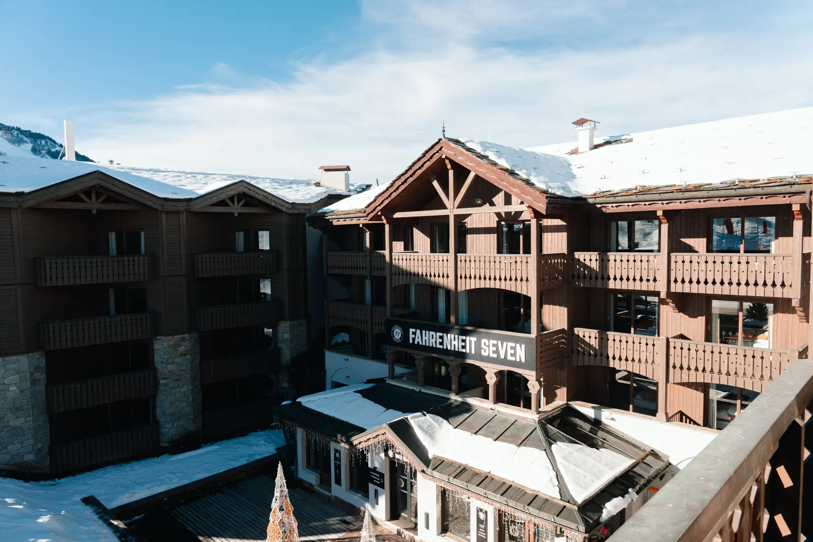 Bâtiment en bois avec balcons sous la neige et un panneau indiquant 'Fahrenheit Seven', sous un ciel bleu clair avec quelques nuages.