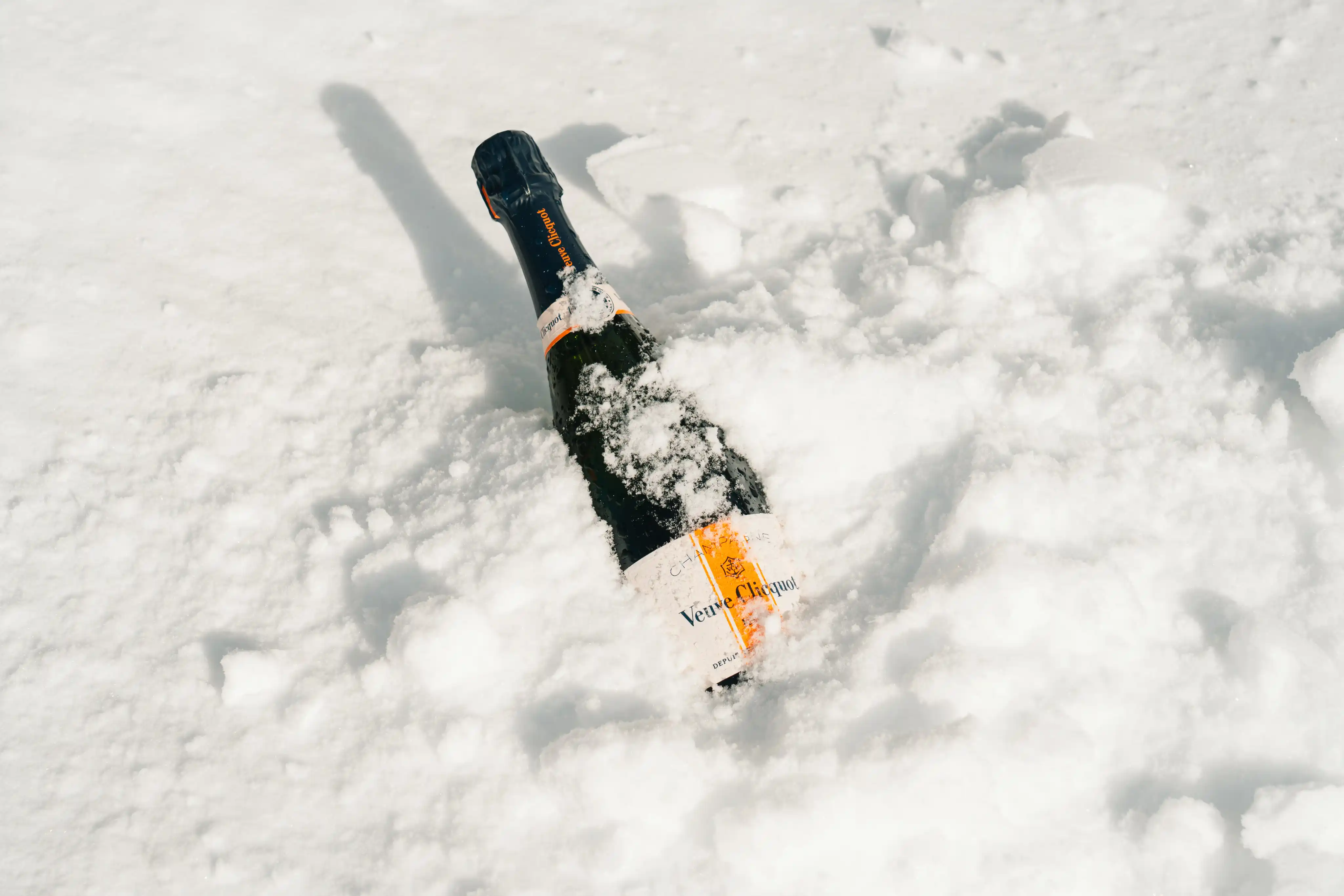 Bouteille de champagne Veuve Clicquot partiellement enfouie dans la neige blanche.