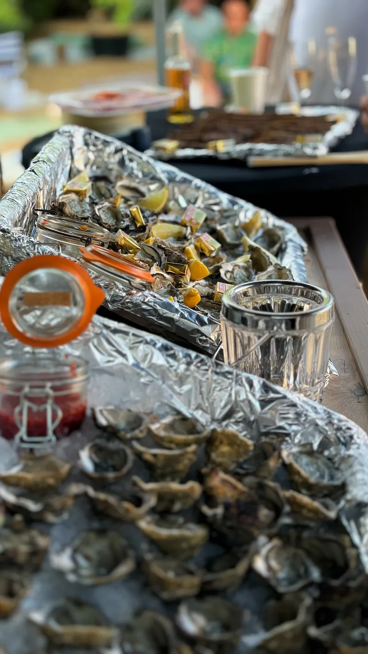 Trays of shucked oysters on ice with lemon wedges and condiments on a wooden table outdoors.