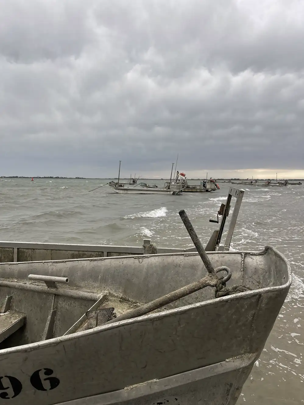 Close-up of a moored gray metal boat with rough sea and cloudy sky in the background.