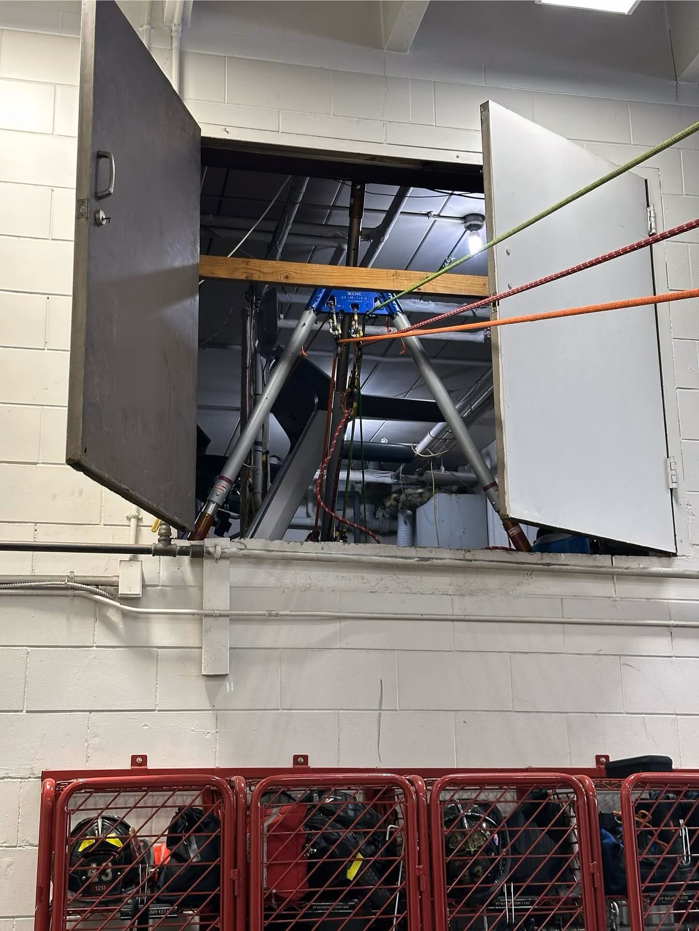 Open wall access panel showing rigging equipment and ropes inside utility space above red storage lockers.
