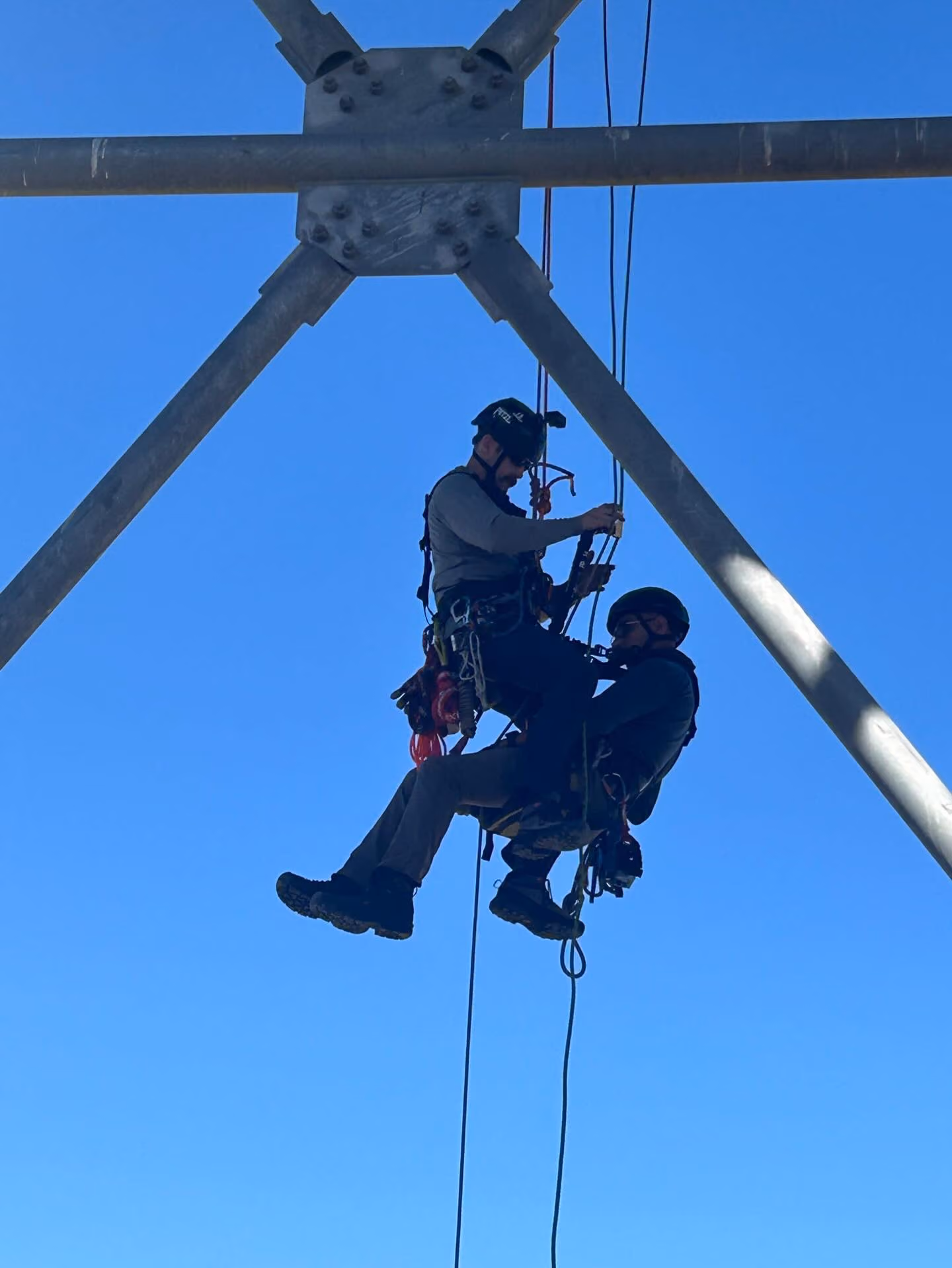 Two rescuers suspended on twin ropes beneath a steel structure