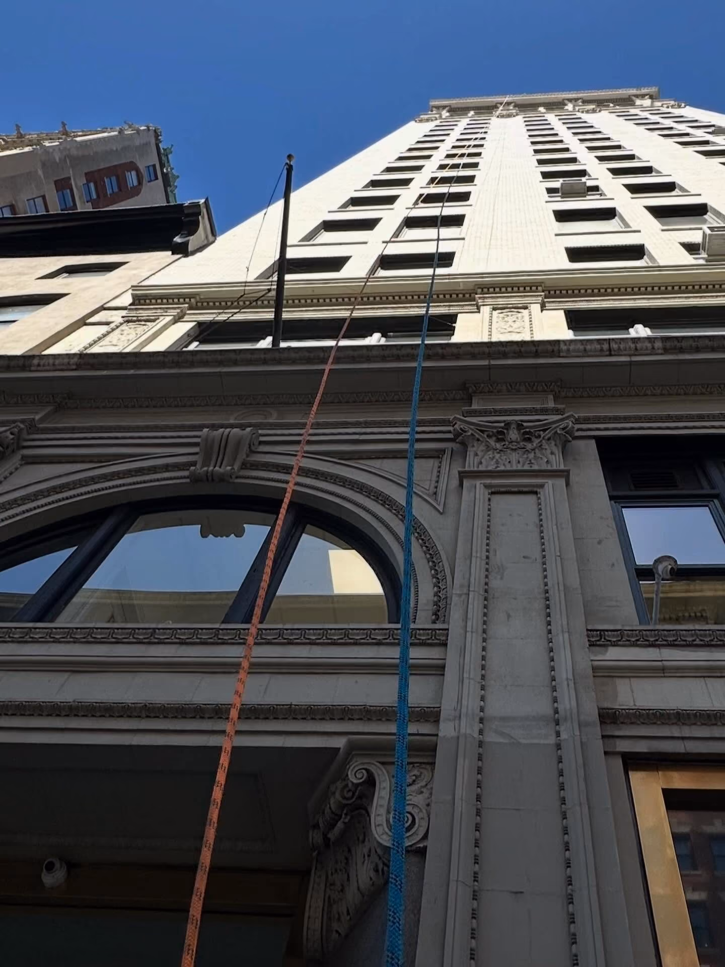 Low-angle view of a tall ornate building with blue sky and two climbing ropes attached near the top.