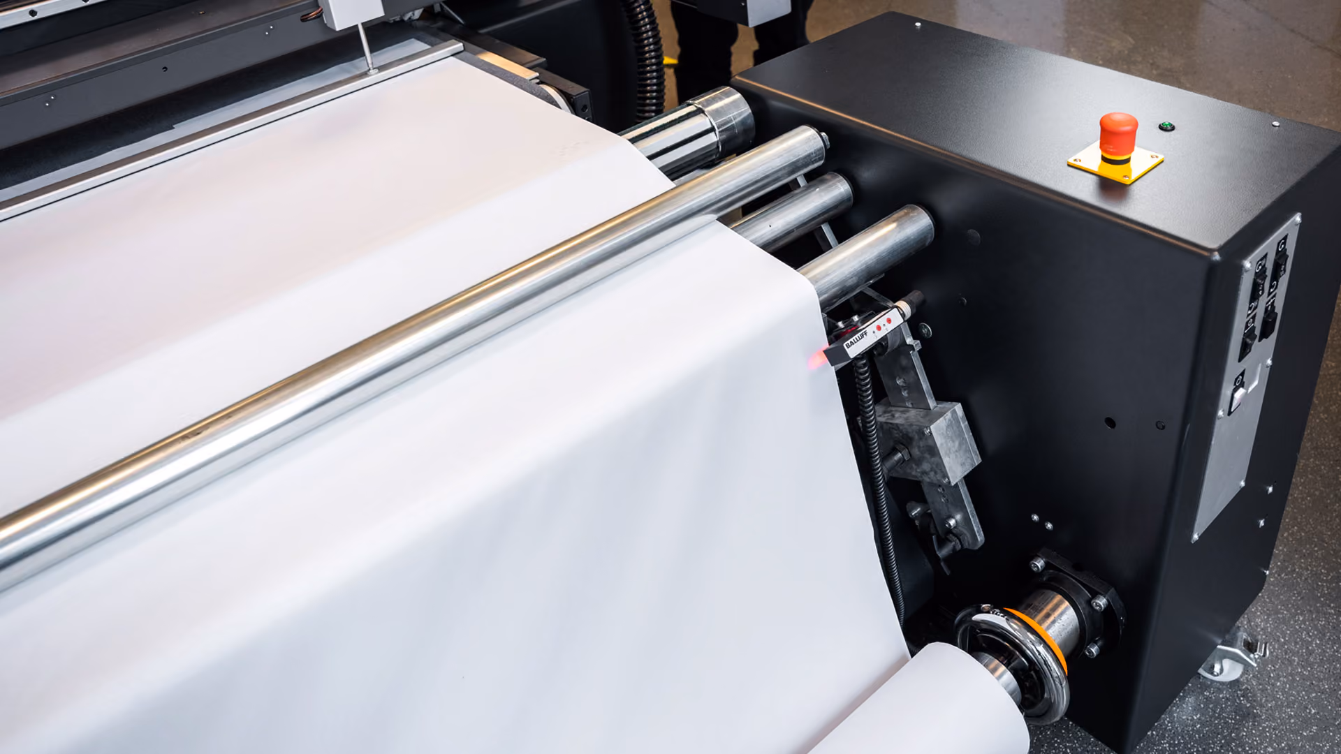 A Kongsberg C64 cutting table being fed a roll of textile material mounted on a Motorized Roll Feeder