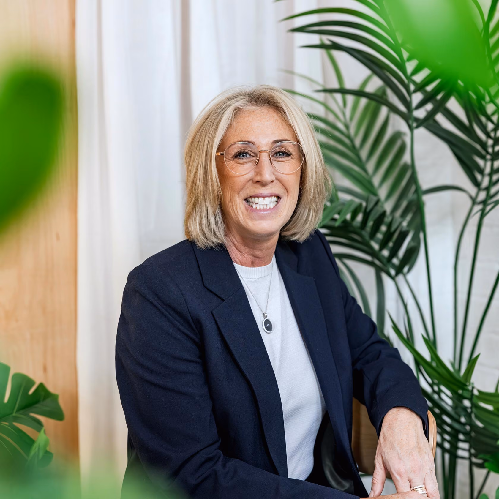 Dr Sarah Carlick smiling as she sits for a photograph against a white brick wall.