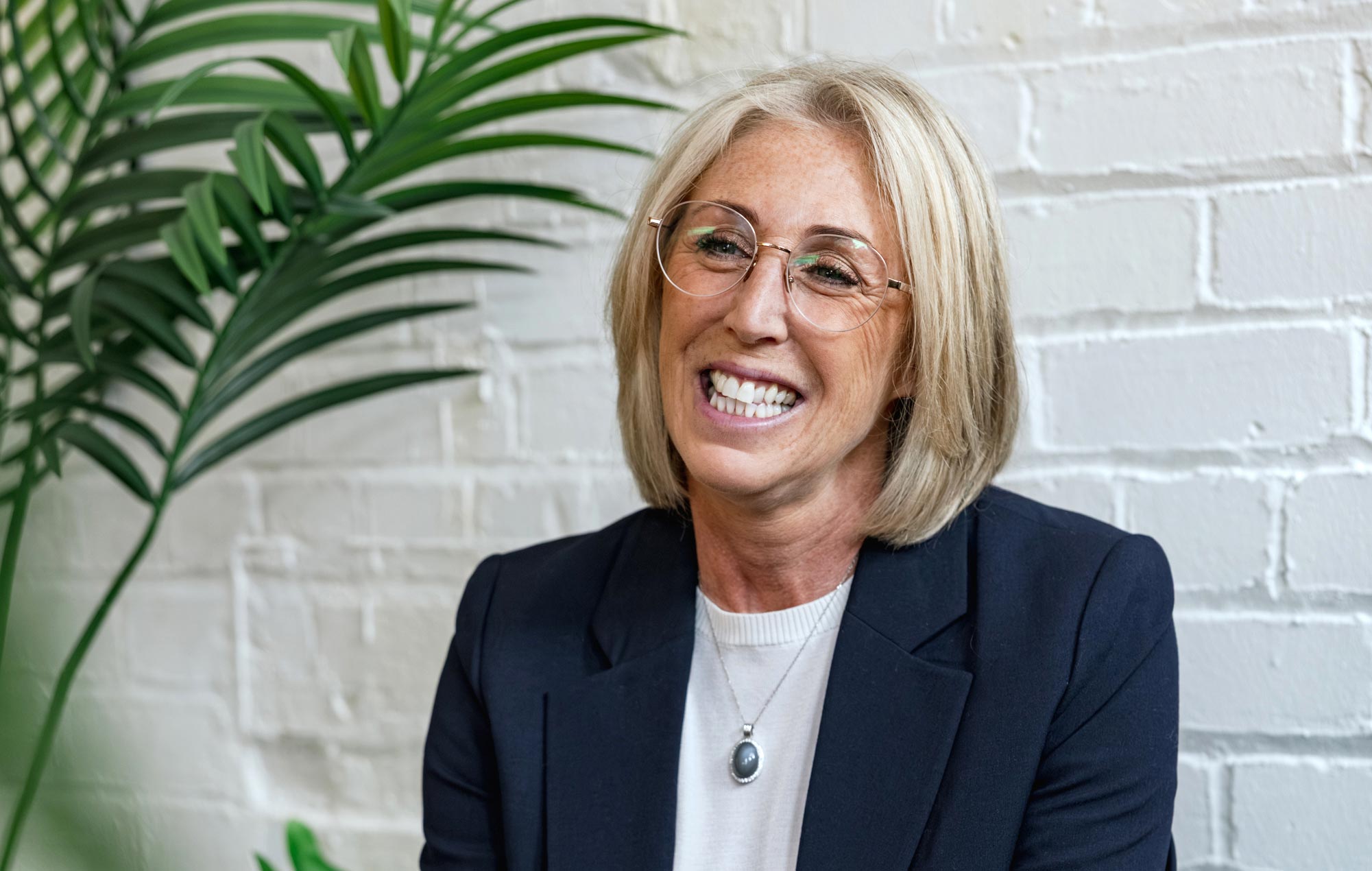 Dr Sarah Carlick smiling as she sits for a photograph against a white brick wall.