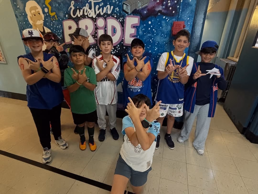 Students in sports jerseys posing in front of the Einstein Pride mural