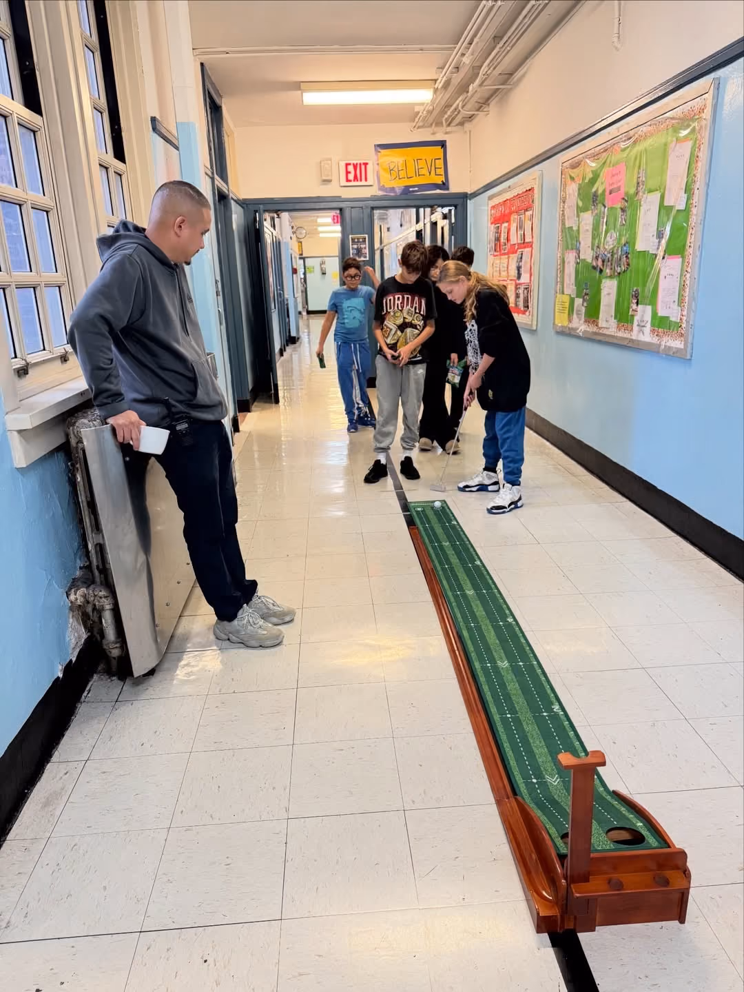 Students taking turns on an indoor putting green in the hallway to earn E-Bucks