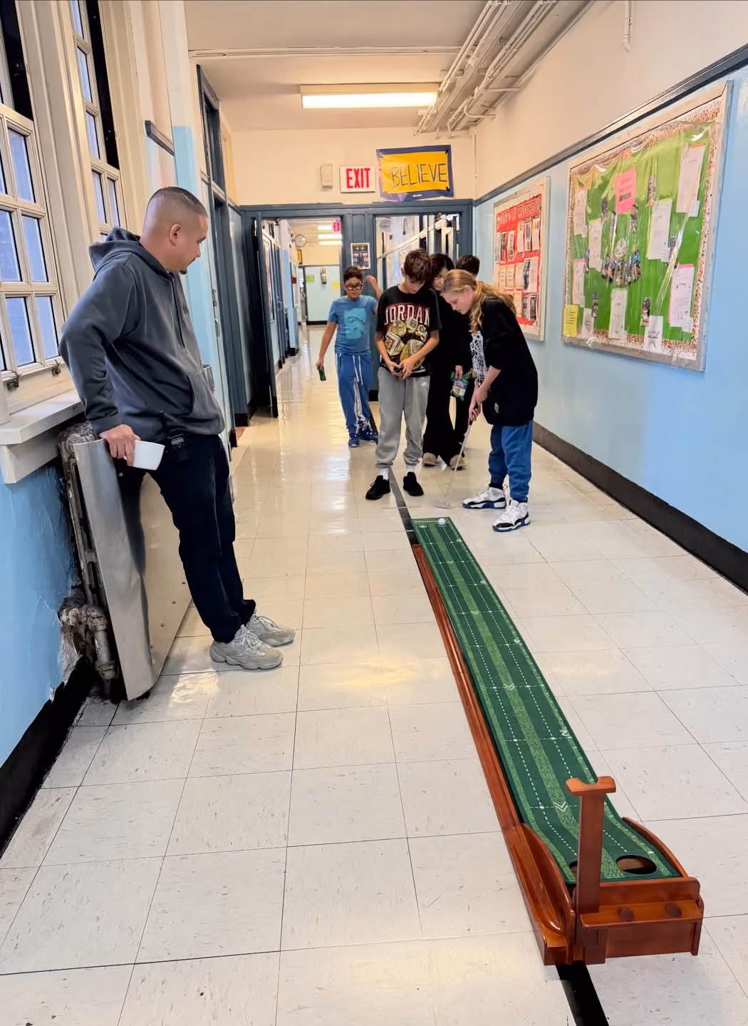 Students taking turns on an indoor putting green in the hallway to earn E-Bucks