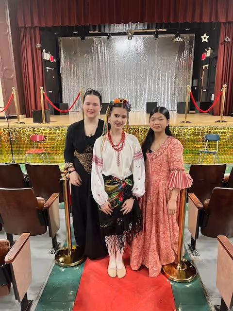 Three students in cultural dress pose in school auditorium