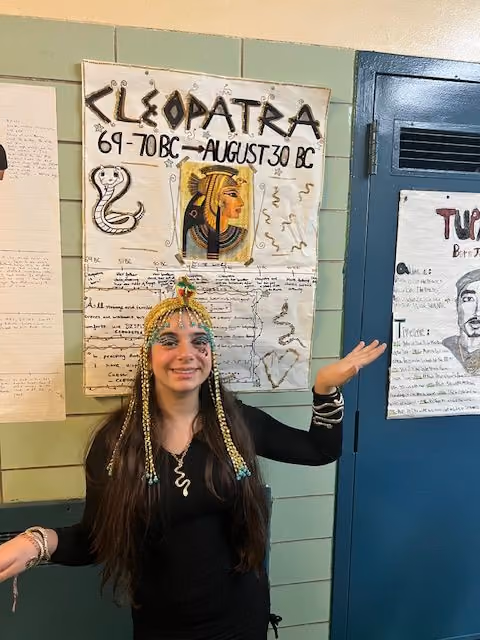 Student dressed as Cleopatra next to her poster for the Living Wax Museum