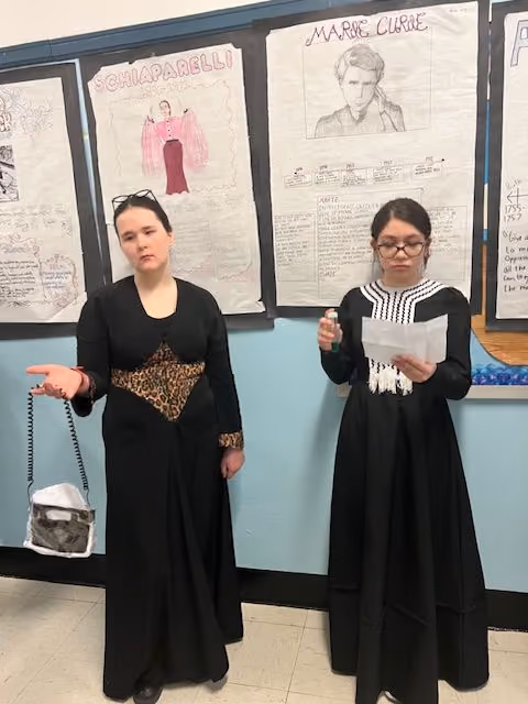 Two students in historical costumes presenting at the Living Wax Museum