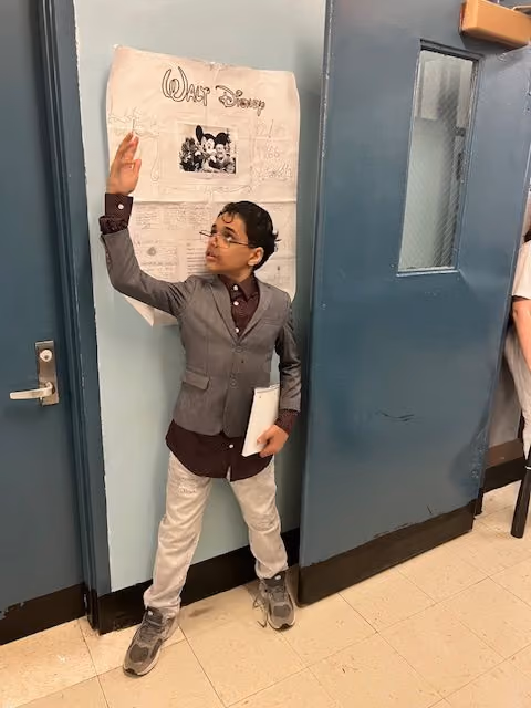 Student dressed as Walt Disney next to his poster for the Living Wax Museum