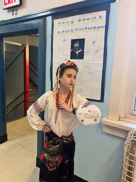 Student in traditional dress posing next to her poster for the Living Wax Museum