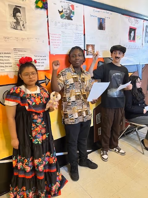 Three students in historical costumes presenting at the Living Wax Museum