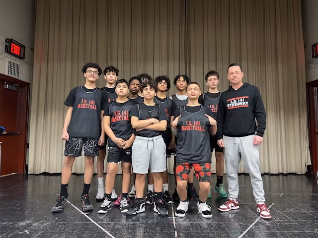 I.S. 141 District 30 middle school basketball team posing on stage with their coach