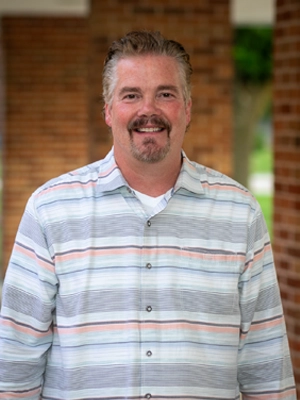 Smiling middle-aged man with short hair and goatee wearing striped button-up shirt.
