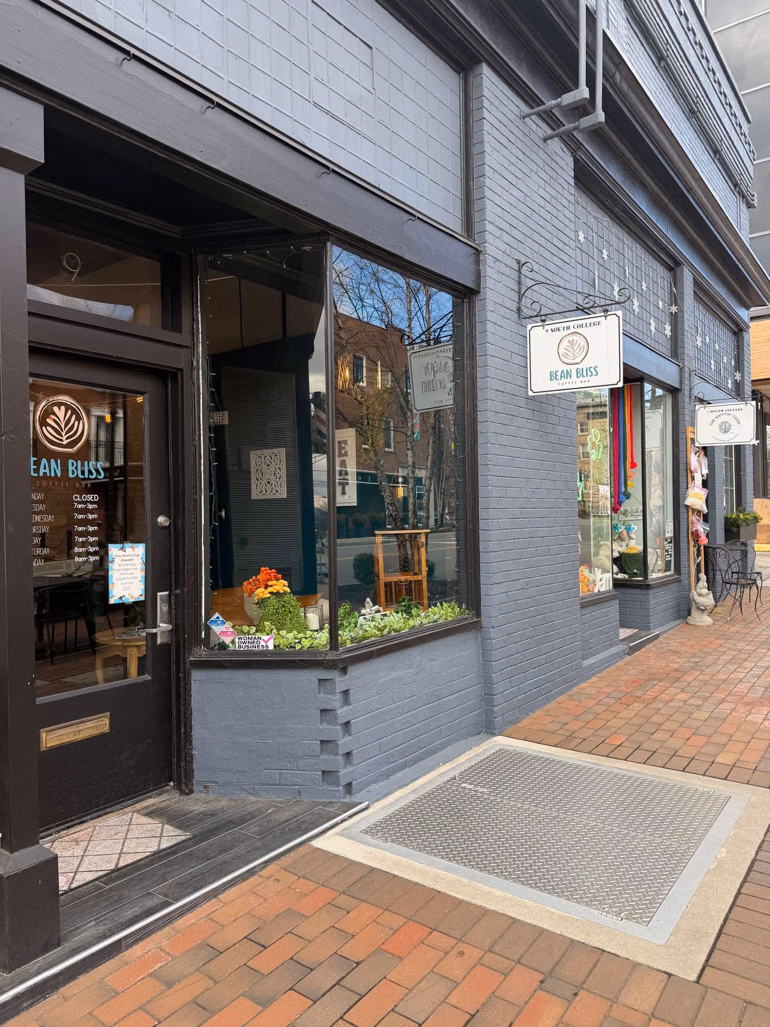 Facade of Bean Bliss Coffee Bar with glass windows, black entrance door, and flower decorations.
