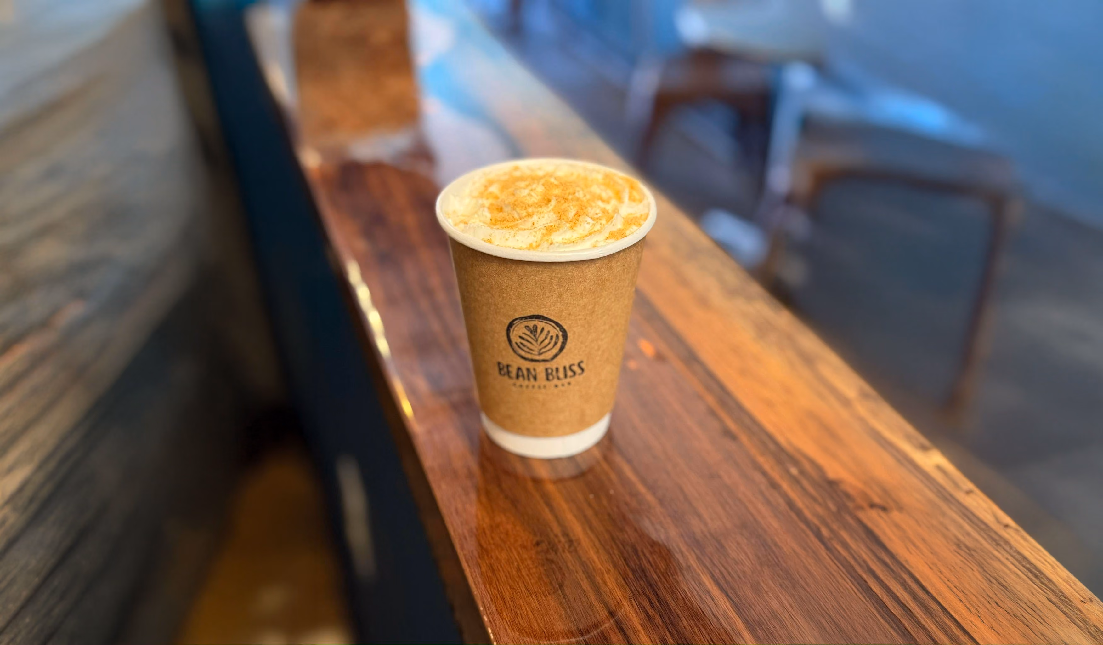 Paper cup of coffee with foam and cinnamon on a wooden counter at Bean Bliss Coffee Bar.