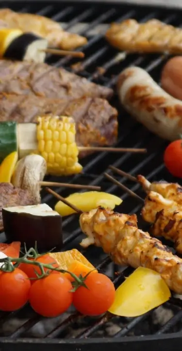 **Alt text:** Assorted grilled lean meats, chicken skewers, sausages, and colorful vegetables cooking on a barbecue grill, highlighting balanced, protein-rich nutrition.