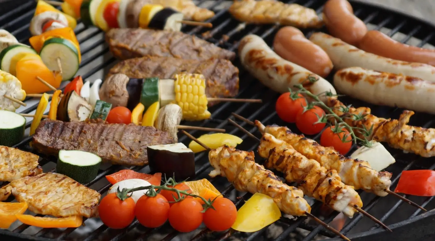 **Alt text:** Assorted grilled lean meats, chicken skewers, sausages, and colorful vegetables cooking on a barbecue grill, highlighting balanced, protein-rich nutrition.