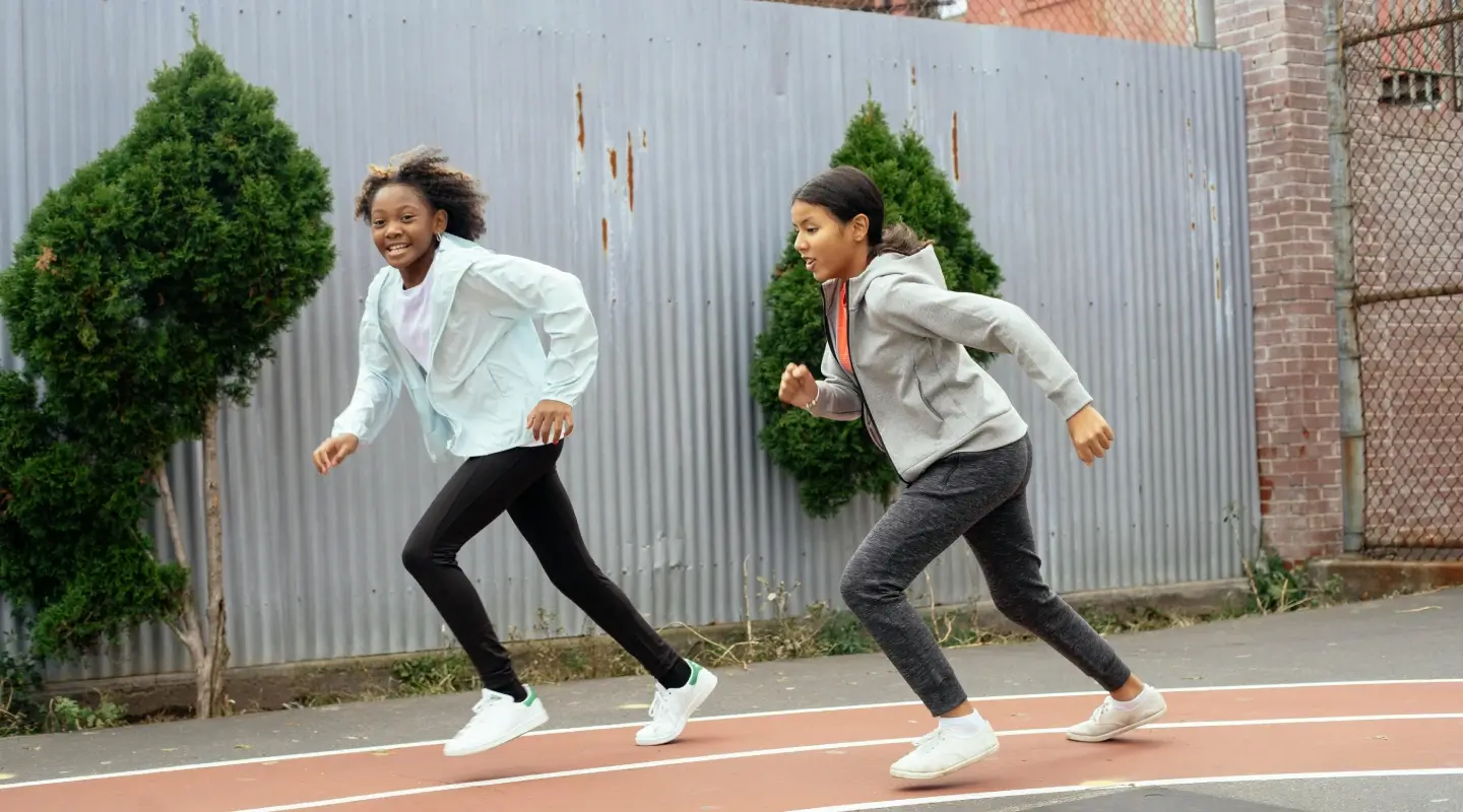 **Alt text:** Young person sprinting on an outdoor running track, wearing athletic clothing and sneakers during a youth fitness training session.