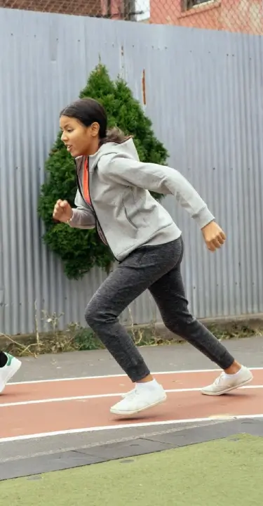 **Alt text:** Young person sprinting on an outdoor running track, wearing athletic clothing and sneakers during a youth fitness training session.