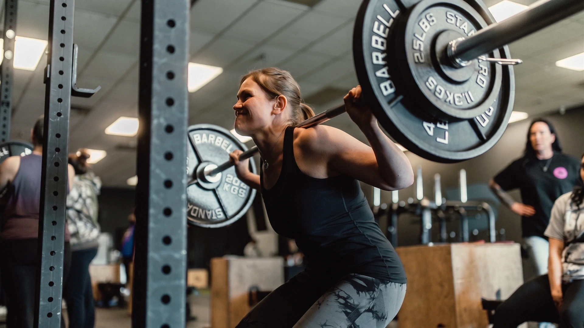 A woman performing a barbell back squat in a gym, focused on her form and strength during training.