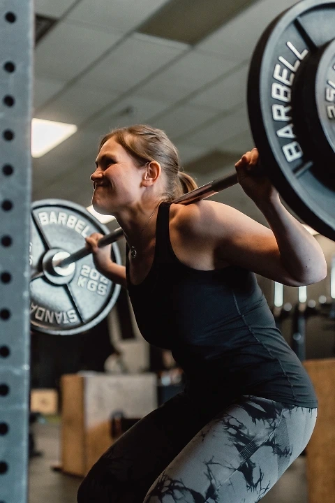 A woman performing a barbell back squat in a gym, focused on her form and strength during training.