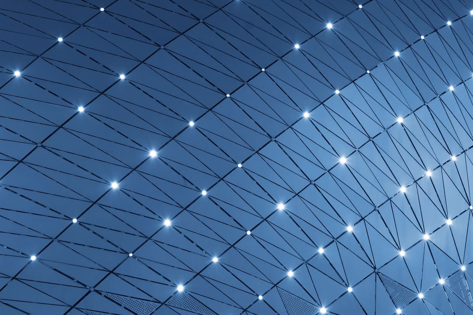 Curved modern glass and metal building facade with diagonal frames and bright white lights.
