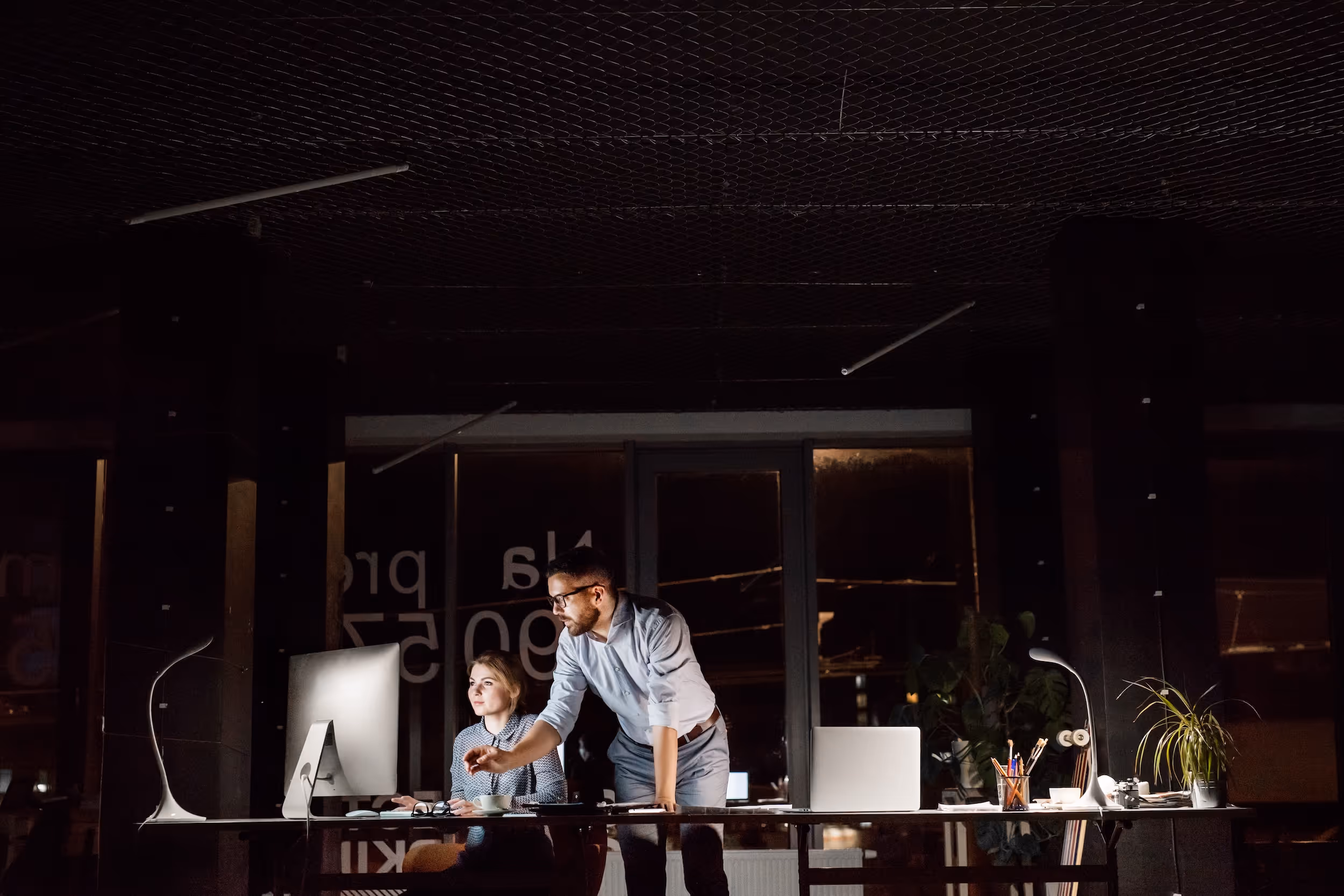 Man and woman working together at a computer in a dimly lit office at night.