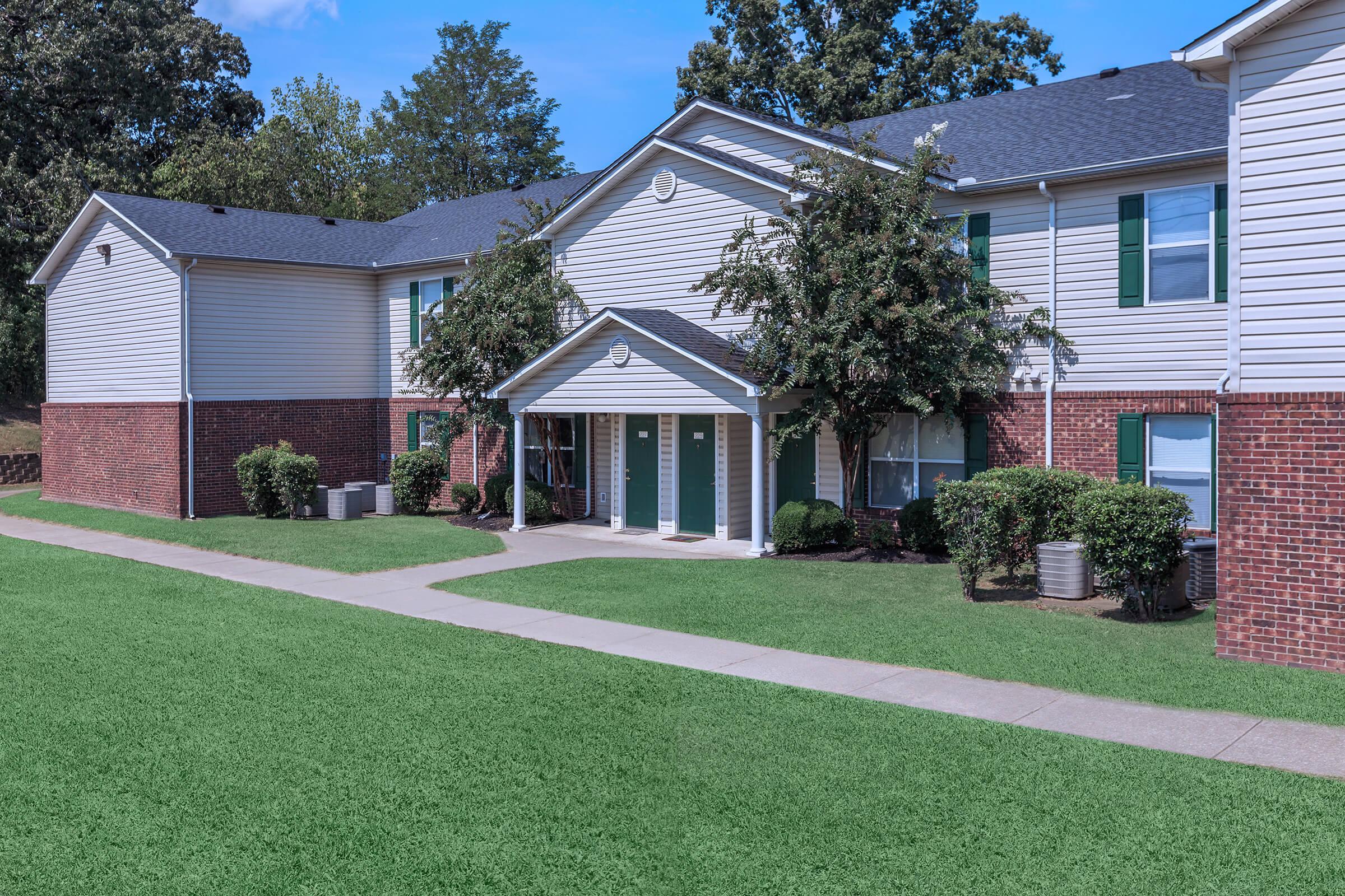 Apartment building exterior with unit entryways surrounded by green landscaping, corner view