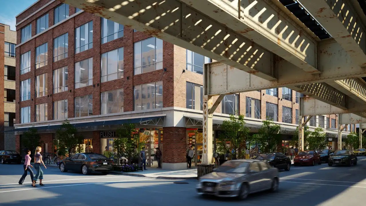 Mixed-use building beneath elevated train tracks in urban setting.