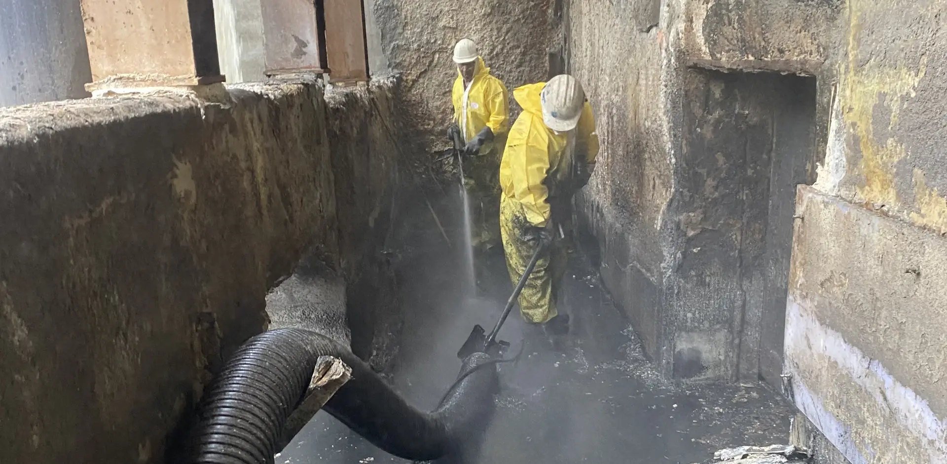 workers spraying industrial site with water hose and shovel