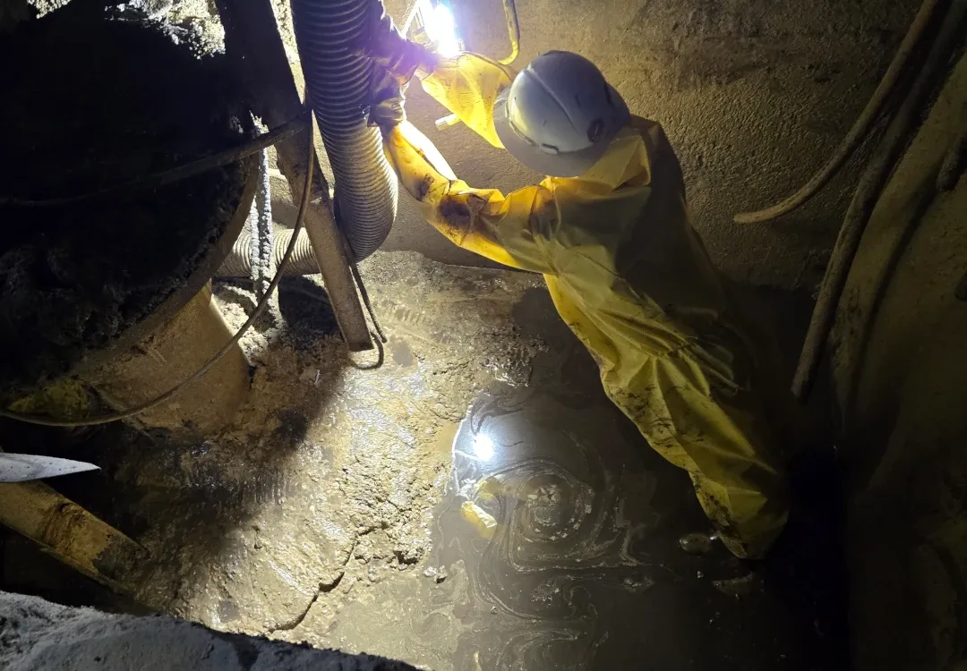 hazmat wearing working in dark tank with puddle of liquid