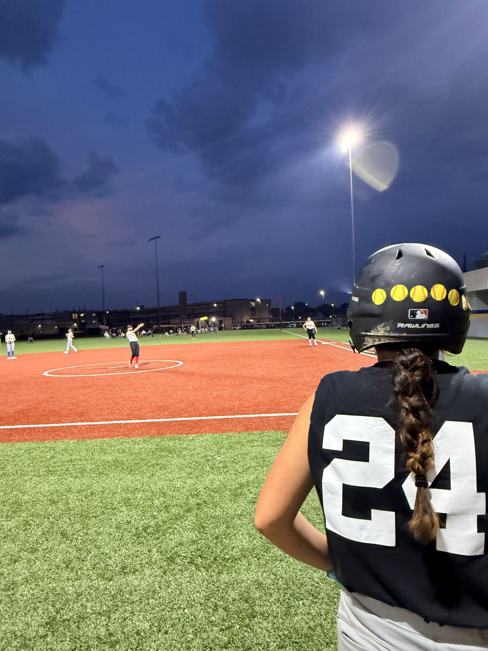 Number 24 watches the field from the dugout at dusk, under the lights.