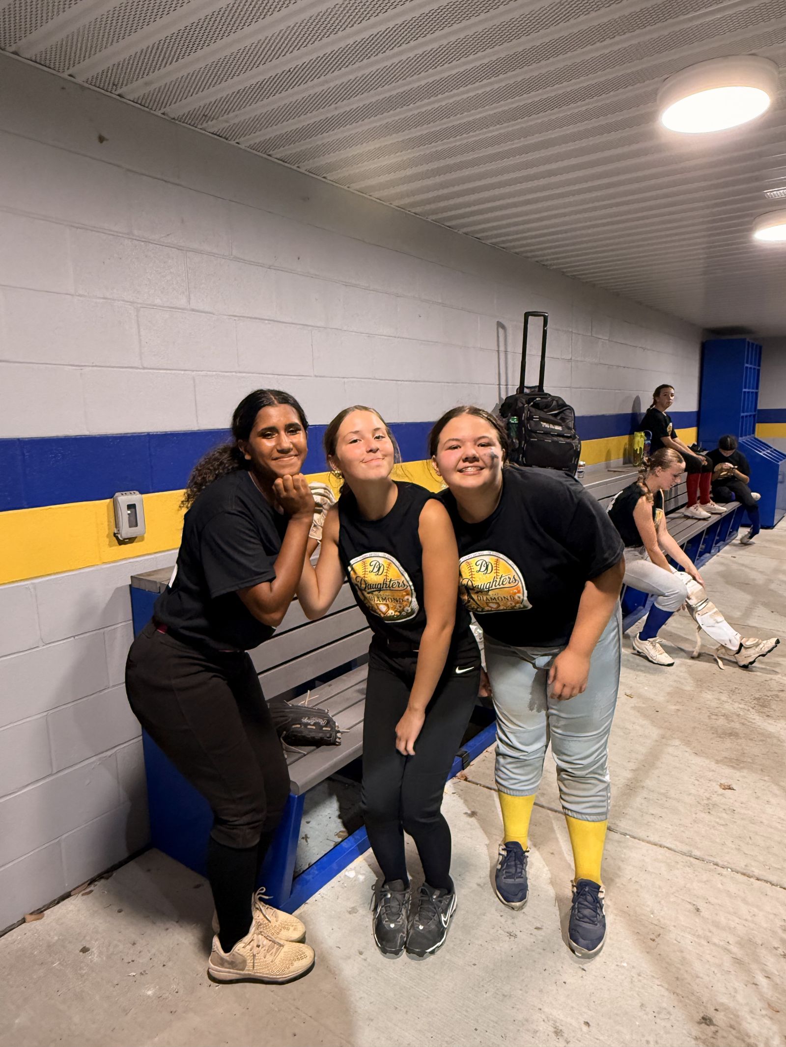 Three teammates laughing together in the dugout.