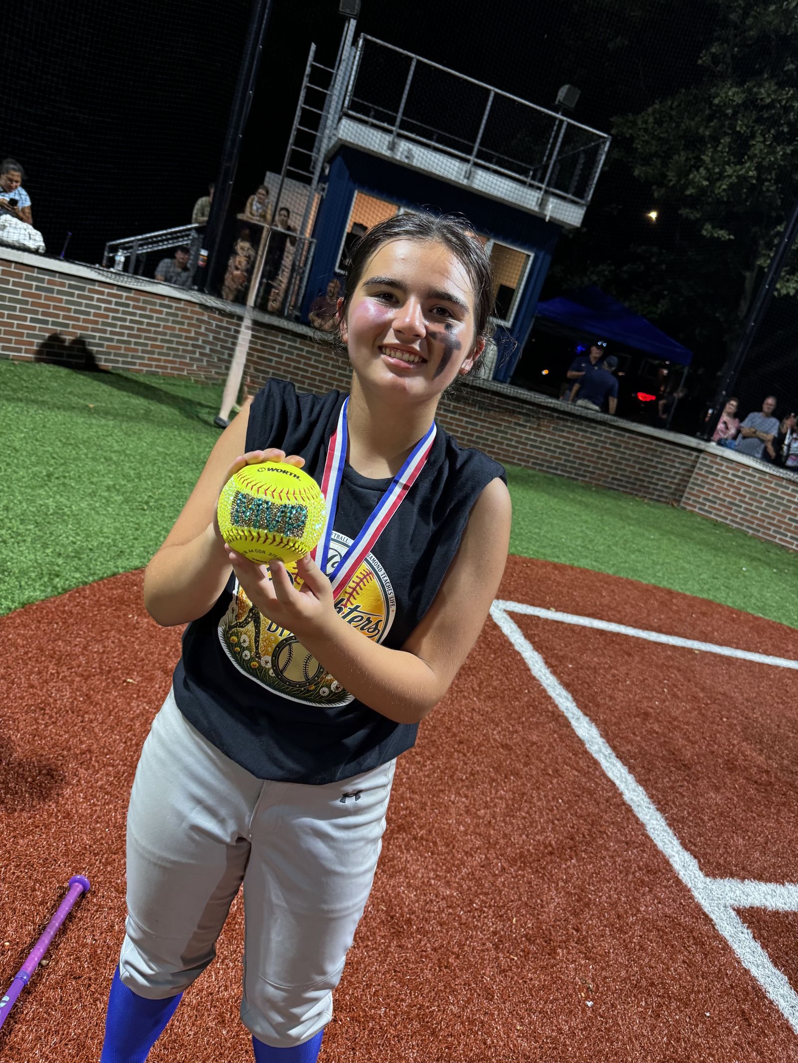 A player holds up her gold softball and medal.