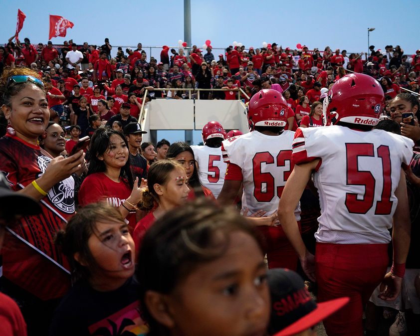 Football players in red uniforms walk through a cheering crowd in a stadium.